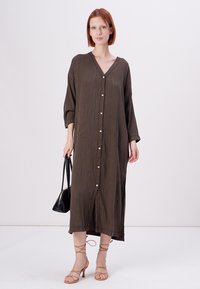 Robe longue vert olive avec un décolleté en V, des boutons sur le devant et des manches trois-quarts. Tissu texturé et silhouette en A.