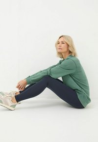 Green sweatshirt, navy leggings, and light sneakers with mint accents. The outfit features soft textures and a relaxed, casual fit.