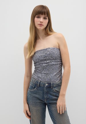 Top plateado brillante sin tirantes con un diseño fruncido, combinado con unos jeans azules desgastados que presentan acentos de puntos en la parte inferior de las piernas.