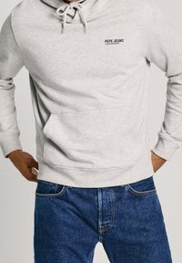 Felpa con cappuccio Pepe Jeans grigio chiaro con tasca frontale e coulisse, indossata con jeans di denim blu, mani appoggiate vicino alla vita.