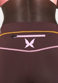 Leggings sportivi color bordeaux con cuciture rosa e arancioni, una piccola tasca con zip e un logo a forma di farfalla rosa sul retro. Texture liscia.