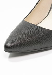 Chaussure plate noire à bout pointu avec dessus en cuir texturé et doublure intérieure beige sur fond blanc.