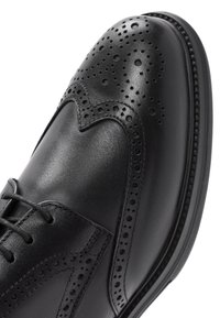Chaussure habillée en cuir noir avec des détails en brogue, texture lisse, conception à lacets et bout rond. Présente des accents perforés et des coutures sur les bords.