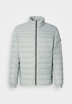 Hellgraue, gepolsterte Jacke mit hohem Kragen, durchgehendem Reißverschluss, gerippten Bündchen und Seitentaschen. Glatte Textur, gesteppte Optik und minimales Zubehör.