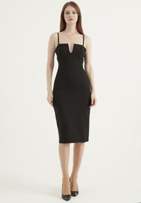 Czarna sukienka midi z dekoltem w serek i cienkimi ramiączkami, o dopasowanym kroju i gładkiej fakturze. Noszona z czarnymi sandałami na obcasie.