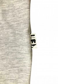 Tessuto grigio a coste con dettagli di trama; presenta un'etichetta bianca con la scritta "KEJO" sul lato.