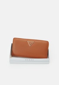 Braune Leder-Brieftasche mit einer strukturierten Oberfläche, ausgestattet mit einem silbernen dreieckigen Logo, präsentiert in einer weißen Box mit einem silbernen "GUESS"-Etikett.