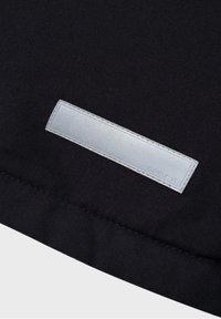 Tissu noir à texture lisse, avec une étiquette rectangulaire argentée centrée et des détails cousus.