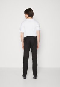 Zwarte broek met een slim fit en een soepele stofstructuur, gecombineerd met een effen wit t-shirt, gezien van achteren.