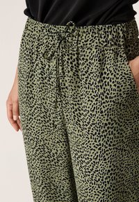 Groene broek met een patroon en een tailleband met trekkoord, voorzien van een zwart abstract ontwerp. De stof lijkt zacht en lichtgewicht, geschikt voor casual gebruik.