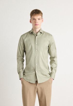 Chemise à manches longues vert clair en tissu tissé, dotée d'un col pointu, d'une fermeture à boutons à l'avant et de poignets simples. Texture unie, sans motifs.