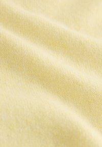 Tissu doux et jaune clair avec une texture en maille fine et des plis délicats créant des ombres subtiles.