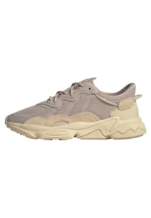 Beżowy sneaker z siateczki i zamszu z teksturowaną kremową podeszwą, wiązany na sznurówki, z falistymi wzorami wzdłuż boków i śródpodeszwy.