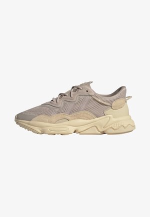 Beżowy sneaker z siateczki i zamszu z teksturowaną kremową podeszwą, wiązany na sznurówki, z falistymi wzorami wzdłuż boków i śródpodeszwy.