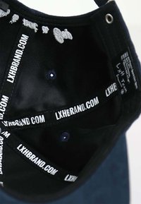 Schwarze Kappe mit Innenfutter und Stoffetiketten in weißem Text. Auffällige Nähdetails und sichtbare Belüftungslöcher. Weiche Textur.
