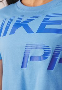 Ljusblå bomulls t-shirt med djupa marinblå bokstäver i ett randigt mönster. Korta ärmar och rund halsringning syns.