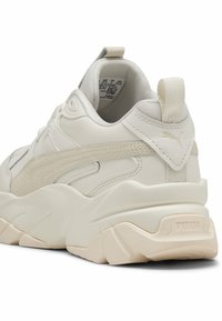 Tömzsi fehér tornacipők bőr és strukturált részletekkel. PUMA logo a sarkon és az oldalon, megerősített orr és párnázott boka rész.