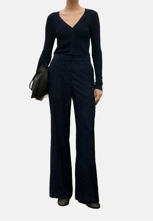 Granatowy kardigan z dekoltem w serek i zapięciem na guziki, zestawiony z wysokim stanem i szerokimi nogawkami spodni. Tkanina o fakturze i dopasowany, strukturalny krój.