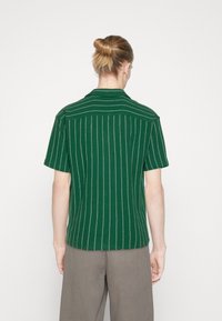 Grön kortärmad skjorta med vertikala vita ränder, med krage, texturerad tyg och en lös passform. Bakvy visas.