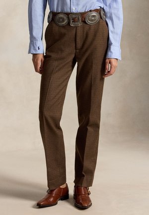 Chemise bleu clair à manches longues rentrée dans un pantalon marron à carreaux avec une large ceinture ornée de grands conchos argentés, associée à des chaussures en cuir marron.
