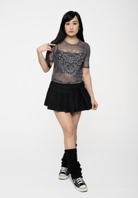 Black sheer mesh top with white graphic design featuring a skull and moth. Paired with a black skirt, leg warmers, and black sneakers.
