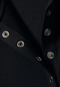 Černá látka s viditelnými druky, s texturovaným povrchem. Druky jsou ze stříbrného kovu s kruhovým designem, dodávají funkční detail.