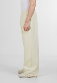 Pantaloni de trening din crem deschis, cu talie elastică, croi drept, buzunare laterale și textură netedă. Purtați cu adidași de culoare deschisă.