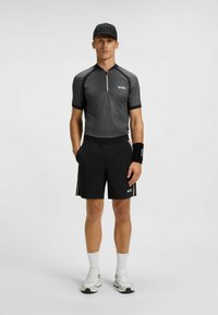 Czarne sportowe szorty z elastycznym pasem, szary t-shirt z krótkim rękawem z złotym zamkiem oraz dopasowana czarna czapka z logo.