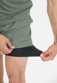 Groene sportshorts met een zwarte binnenlaag. De shorts hebben een gladde textuur, logo-details en een lichtgewicht ontwerp.