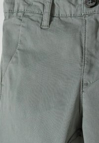 Pantaloni in misto cotone verde chiaro con una superficie liscia, tasche anteriori e chiusura a bottone con dettagli di cucitura in vita.