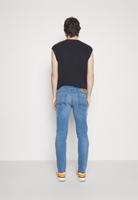 Top de punto sin mangas en negro con textura acanalada, combinado con jeans de mezclilla ajustados en azul claro que incluyen detalles en los bolsillos traseros y una etiqueta de marca.