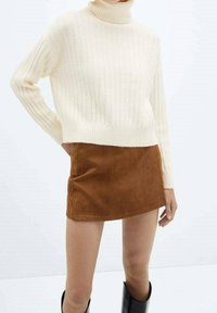 Maglione a collo alto a costine di colore crema abbinato a una mini gonna in suede marrone. L'insieme presenta una texture accogliente e una silhouette aderente. Stivali neri al ginocchio.