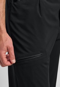 Zwarte sportbroek met een ritssluiting aan de zijkant, gemaakt van gladde, lichte stof met een aansluitend ontwerp.