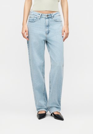 Világoskék, magas derekú, egyenes szárú farmernadrág fekete, hegyesorrú magassarkú cipővel és egy rövidített, világoszöld ujjatlan felsővel viselve.