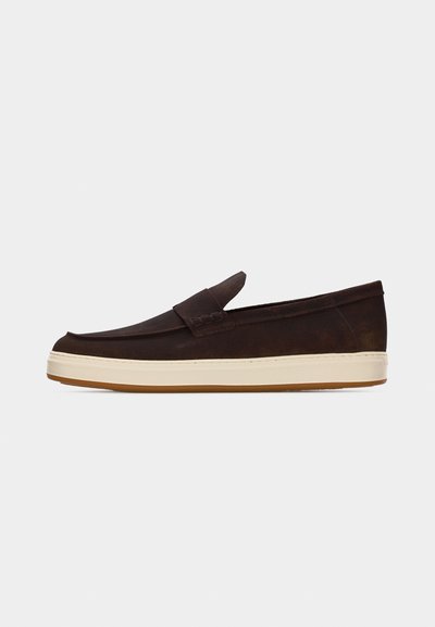 Mocassin à enfiler en daim brun foncé avec semelle en caoutchouc crème et détails de couture minimalistes, présenté de profil sur un fond clair uni.
