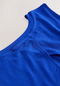 Gros plan d'un haut de sport bleu montrant l'encolure et les détails des coutures sur un fond clair.