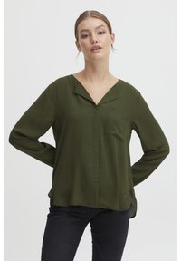 Blusa verde a maniche lunghe in tessuto leggero con scollatura a V, taschino sul petto e orlo curvo, caratterizzata da sottili spacchi laterali e dettagli di branding.