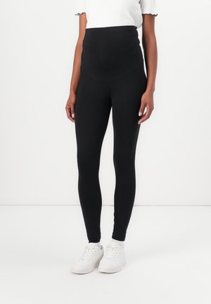Zwarte high-waisted leggings van rekbare stof, met een gladde textuur en een aansluitend ontwerp. Draag ze met witte sneakers.