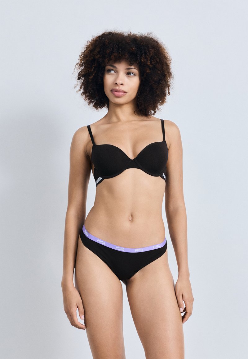 Brassiere negro con copas moldeadas, tirantes finos y acentos de logo. Braguitas negras con una cinturilla morada que presenta el logo de la marca. Textura de tela suave.
