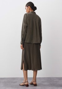 Olive green, linen shirt and matching skirt. Shirt features a back yoke; skirt includes a side slit. Sandals with thin straps and block heels.