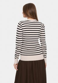 Gestreifter Pullover in Creme und Schwarz, mit tailliertem Design, gerippten Bündchen und Rundhalsausschnitt, kombiniert mit einem braunen Rock.