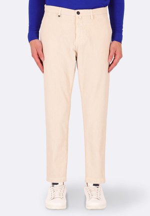 Pantaloni a righe beige con taglio dritto, dotati di chiusura a bottone, passanti per cintura e tasche laterali, abbinati a sneaker bianche.