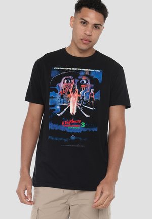 Young man wearing black t-shirt with colorful "A Nightmare on Elm Street 3: Dream Warriors" movie poster featuring four characters and a large face.