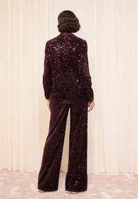 Costum din sacou și pantaloni burgund cu paiete, având o textură fină și un design cu picioare largi, cu guler în formă de cioc și mâneci lungi.
