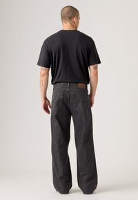 Black t-shirt and loose-fit gray denim jeans. The jeans have a classic five-pocket design and a leather back patch.