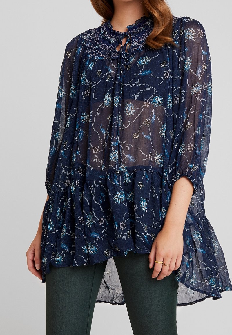 Námořnická květinová blůza s jemným krajkovým límcem, průhlednou tkaninou, dlouhými rukávy a vrstveným lemem. Obsahuje modré a bílé květinové vzory.