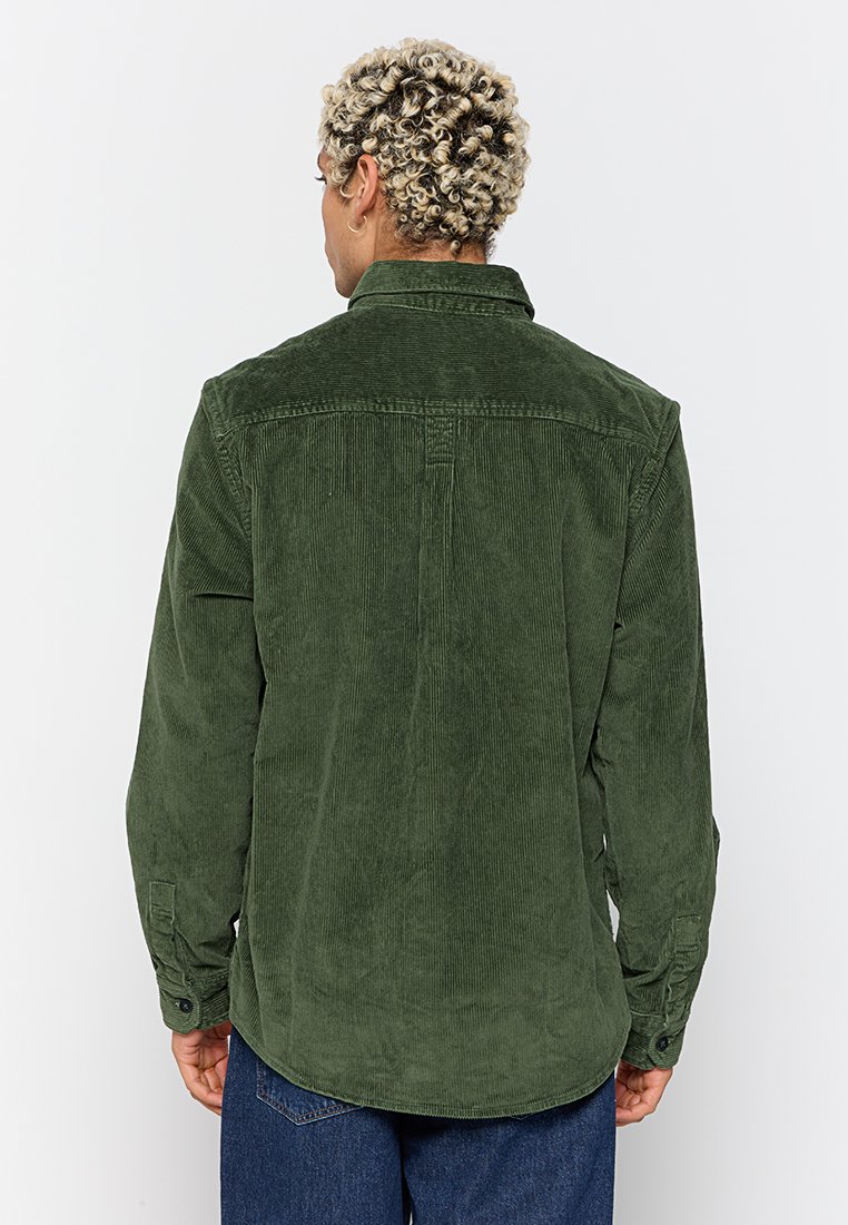 Camicia a righe verdi in corduroy con maniche lunghe, colletto abbottonato e dettaglio dello yoke posteriore. Presenta un tessuto testurizzato e un orlo arrotondato.