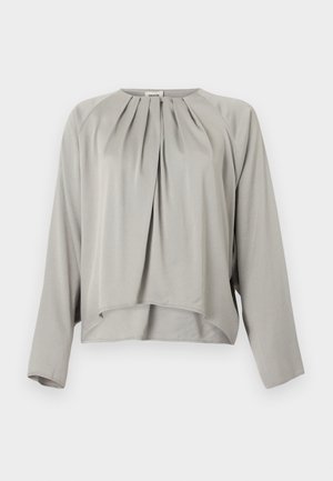 Svetlo siva bluza z dolgimi rokavi z okroglim izrezom, sprednjimi gubami in rahlo asimetričnim spodnjim robom.