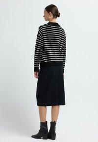 Maglione a righe bianche e nere con una vestibilità morbida, abbinato a una gonna midi in denim nera. Stivali alla caviglia neri completano il look.
