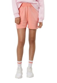 Pantaloni sportivi color pesco con vita elasticizzata, abbinati a sneakers bianche e calze a righe coordinate. Materiale in cotone morbido.